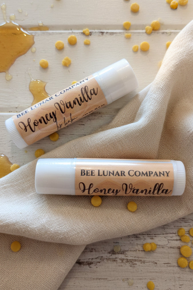 Two lip balm tubes with 'Bee Lunar Company' label on a light wooden surface