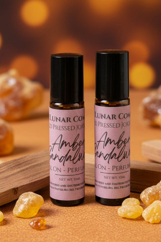 Two roll on  Bee Lunar Company Amber Sandalwood perfume oils with amber resins on a wooden surface.